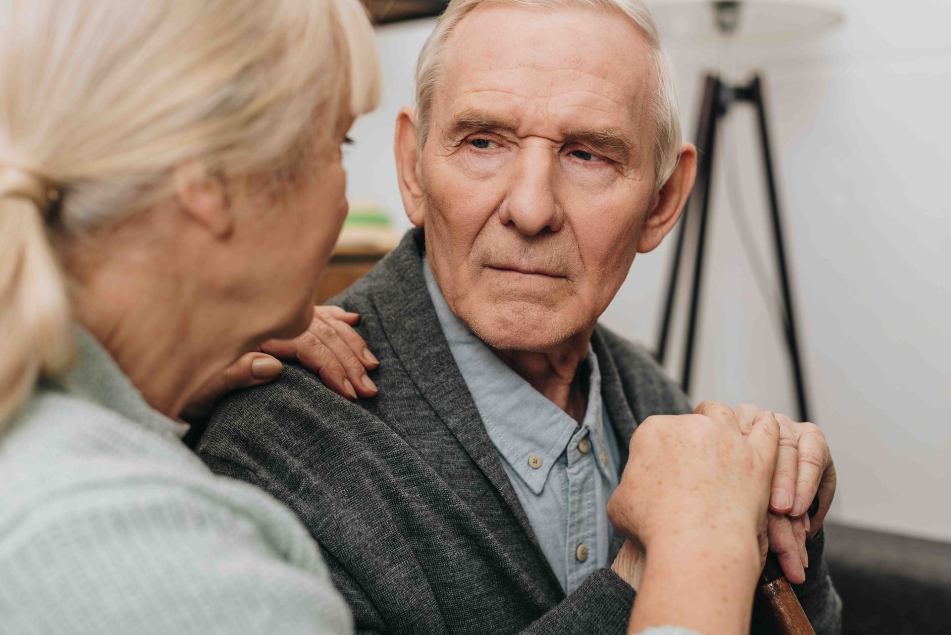 An elderly couple is holding hands and looking at each other.