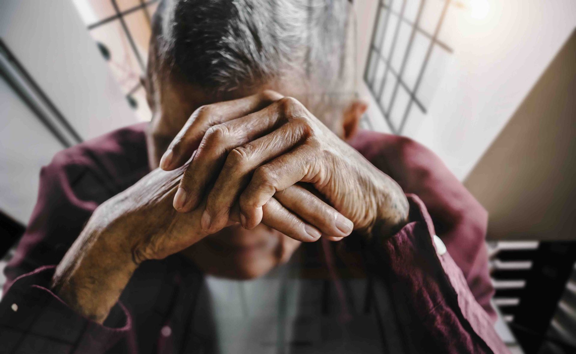 An older man is covering his face with his hands.