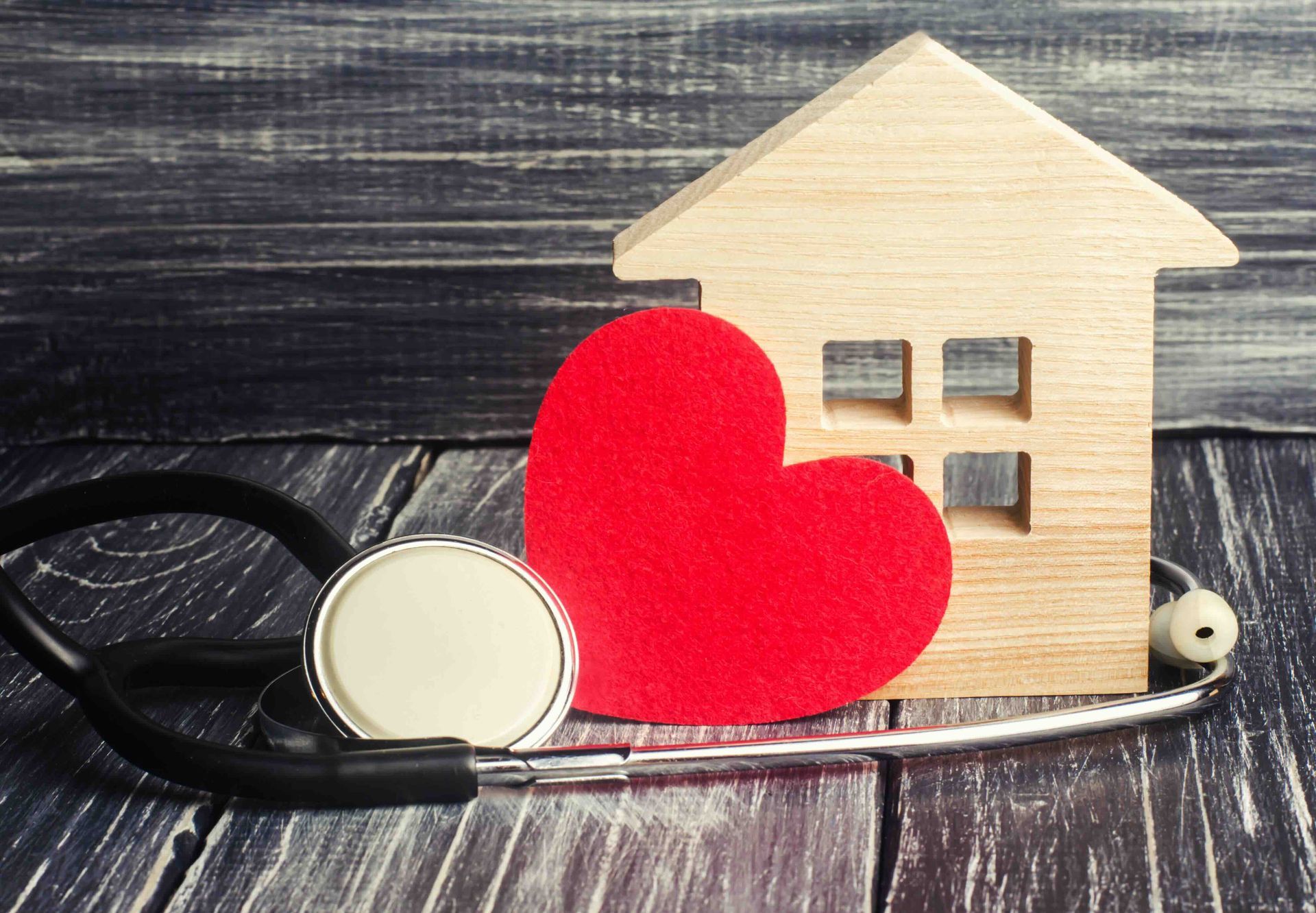 A wooden house with a red heart and a stethoscope on a wooden table.