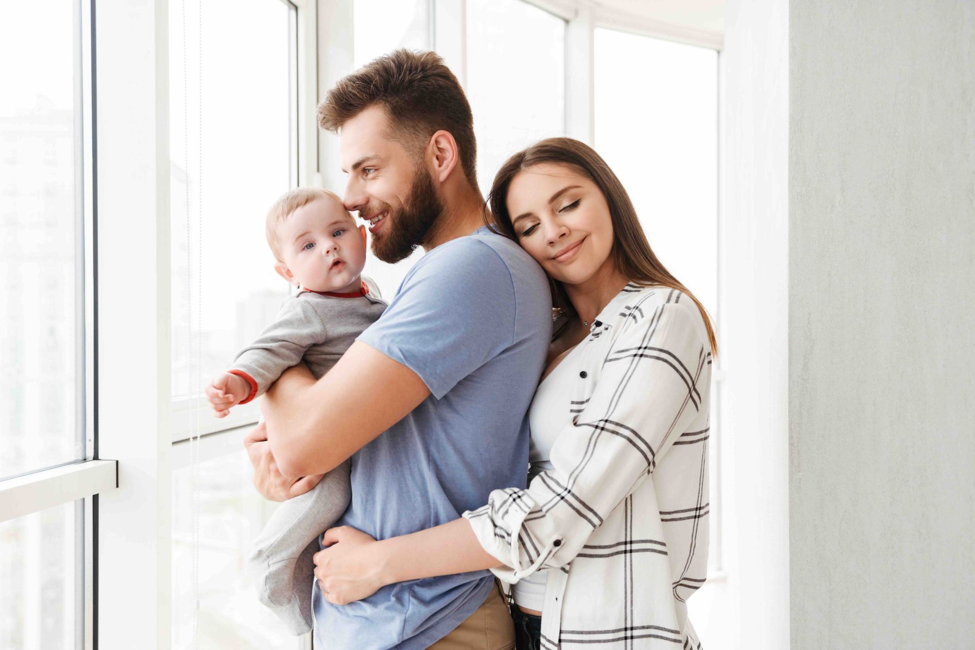 A man and a woman are holding a baby in front of a window.