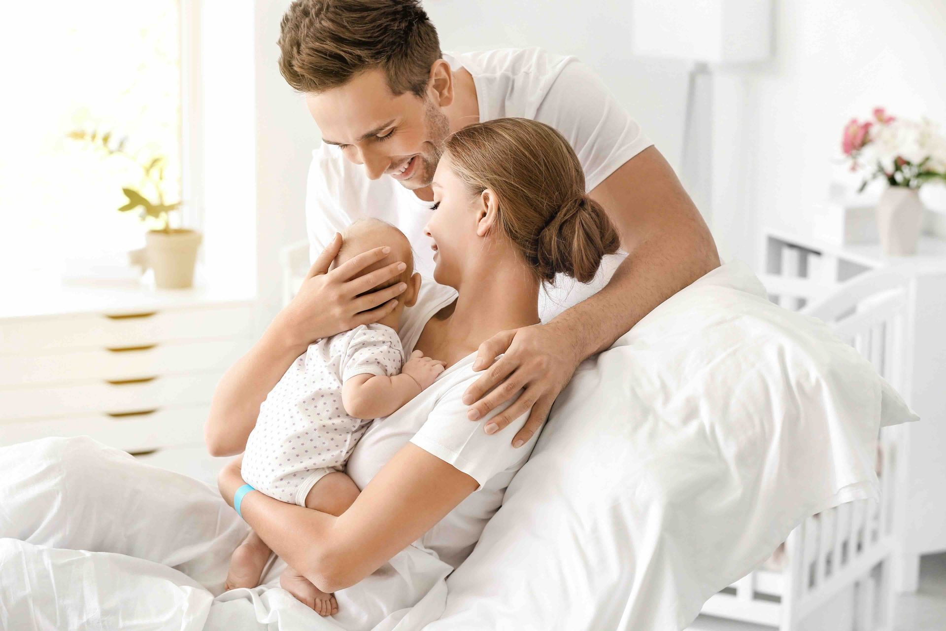 A man and a woman are holding a baby while sitting on a bed.