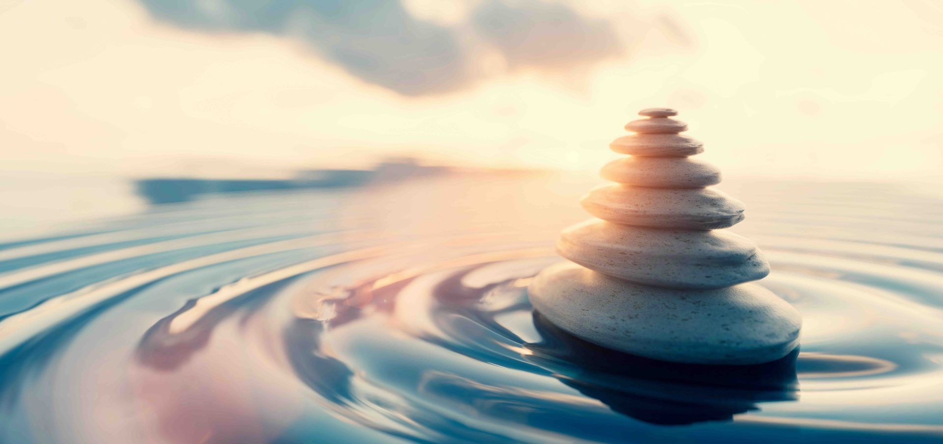 Stack of stones on water ripples, with a blurred ocean and sky in the background.
