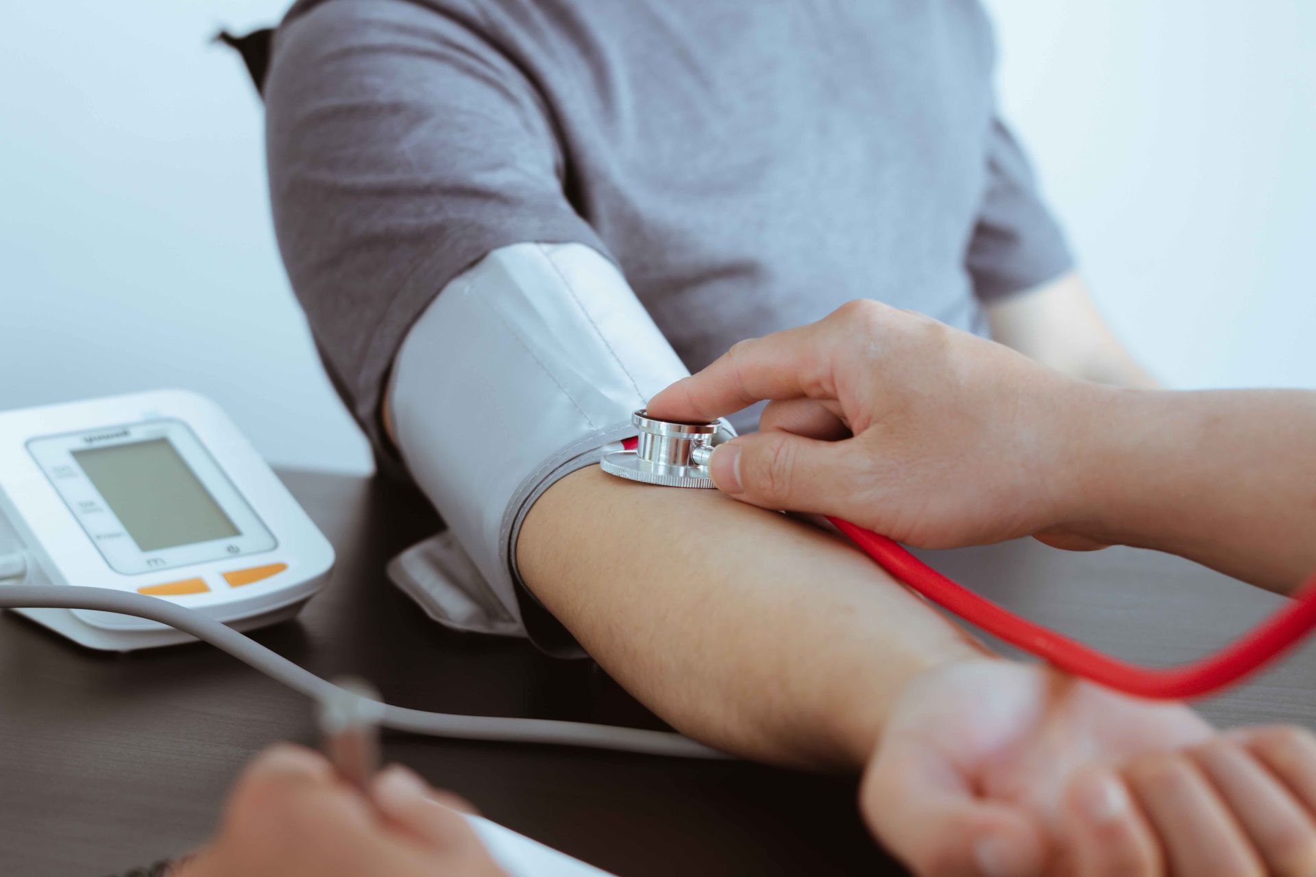 Person having their blood pressure checked at a desk. A cuff is on their arm, and a stethoscope is used.