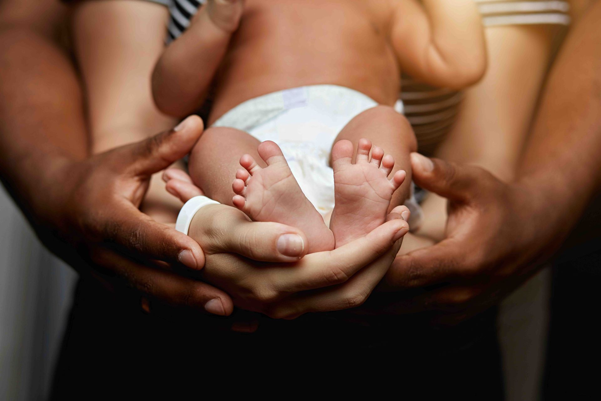 Adults holding a newborn baby’s feet in their hands.