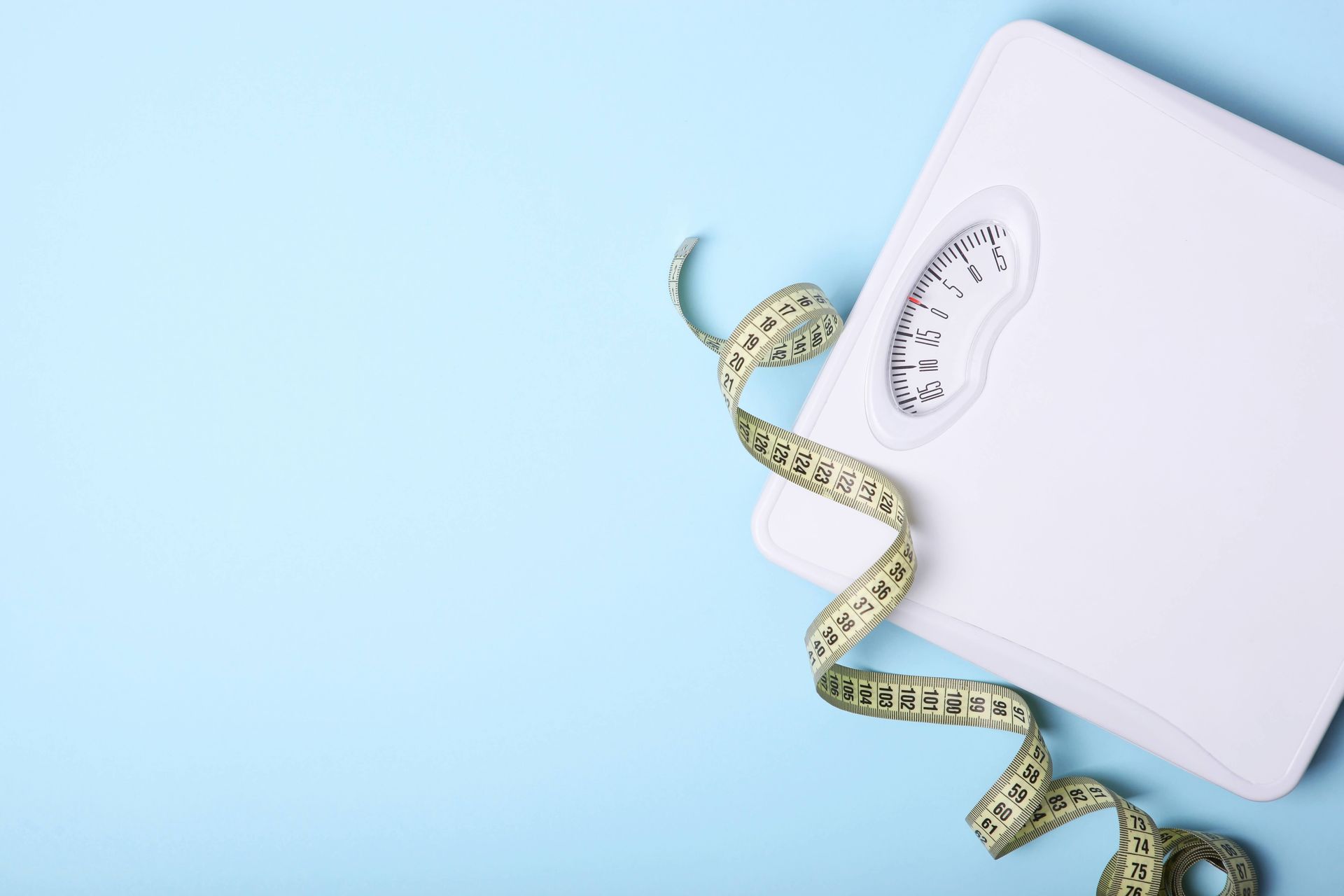 A white scale with a measuring tape attached to it on a blue background.