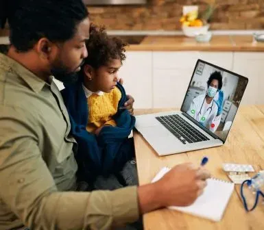 A man is sitting at a table with a child and a laptop.