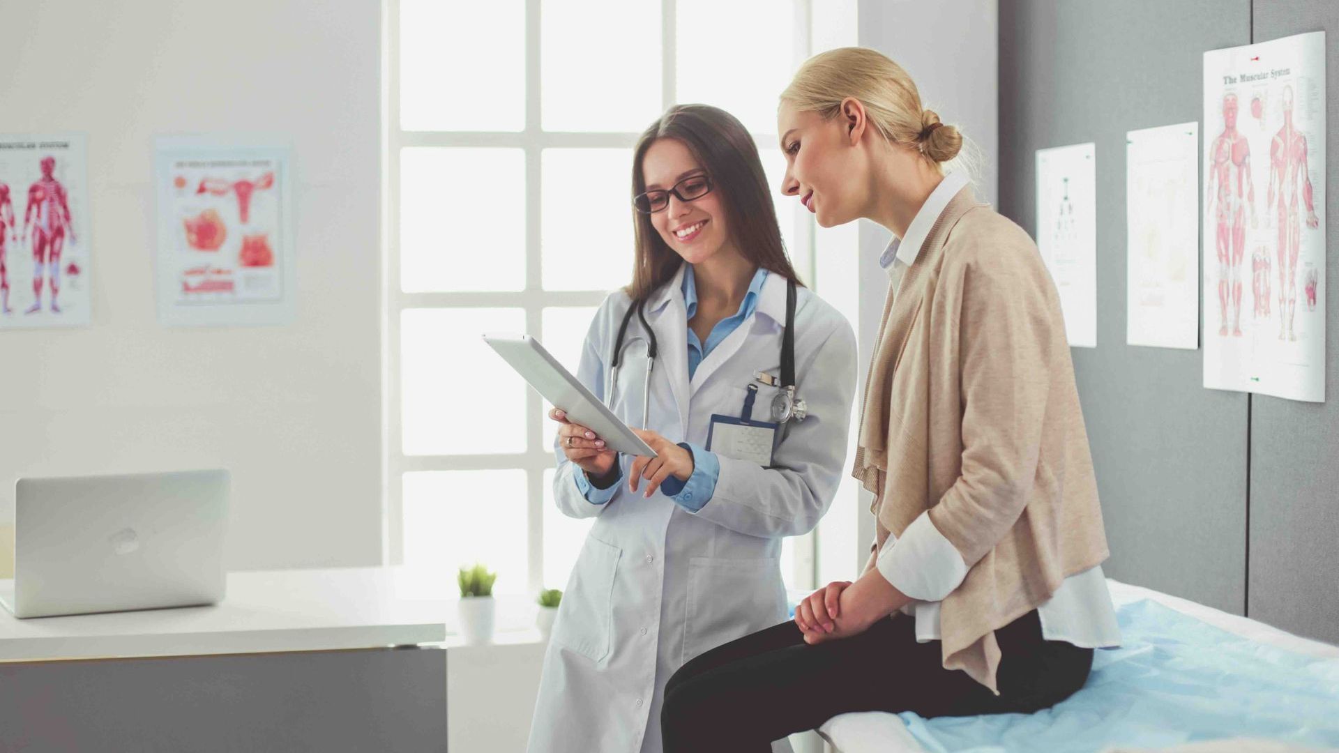 a doctor is talking to a female patient who is sitting on a bed.