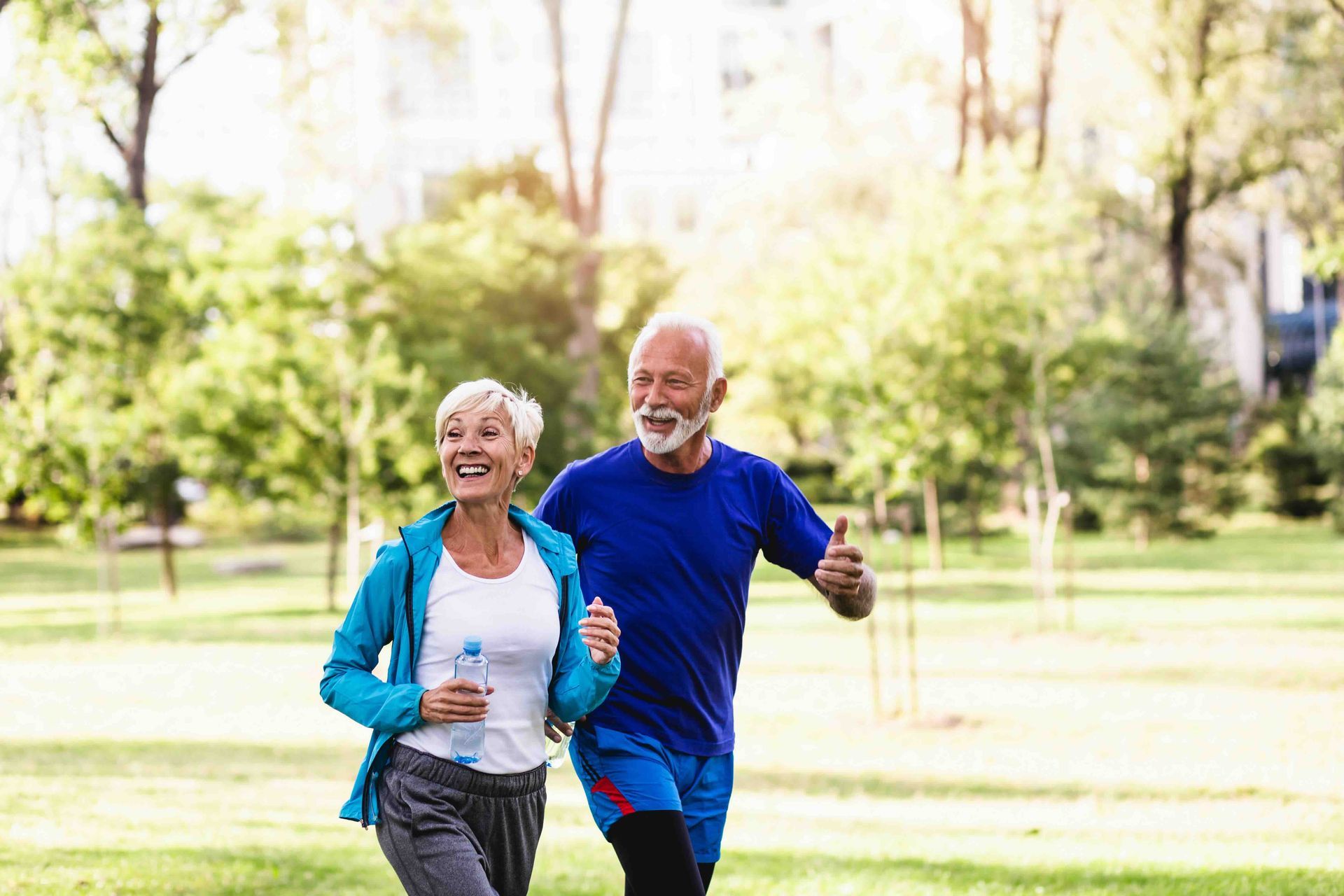 An elderly couple is jogging in a park.