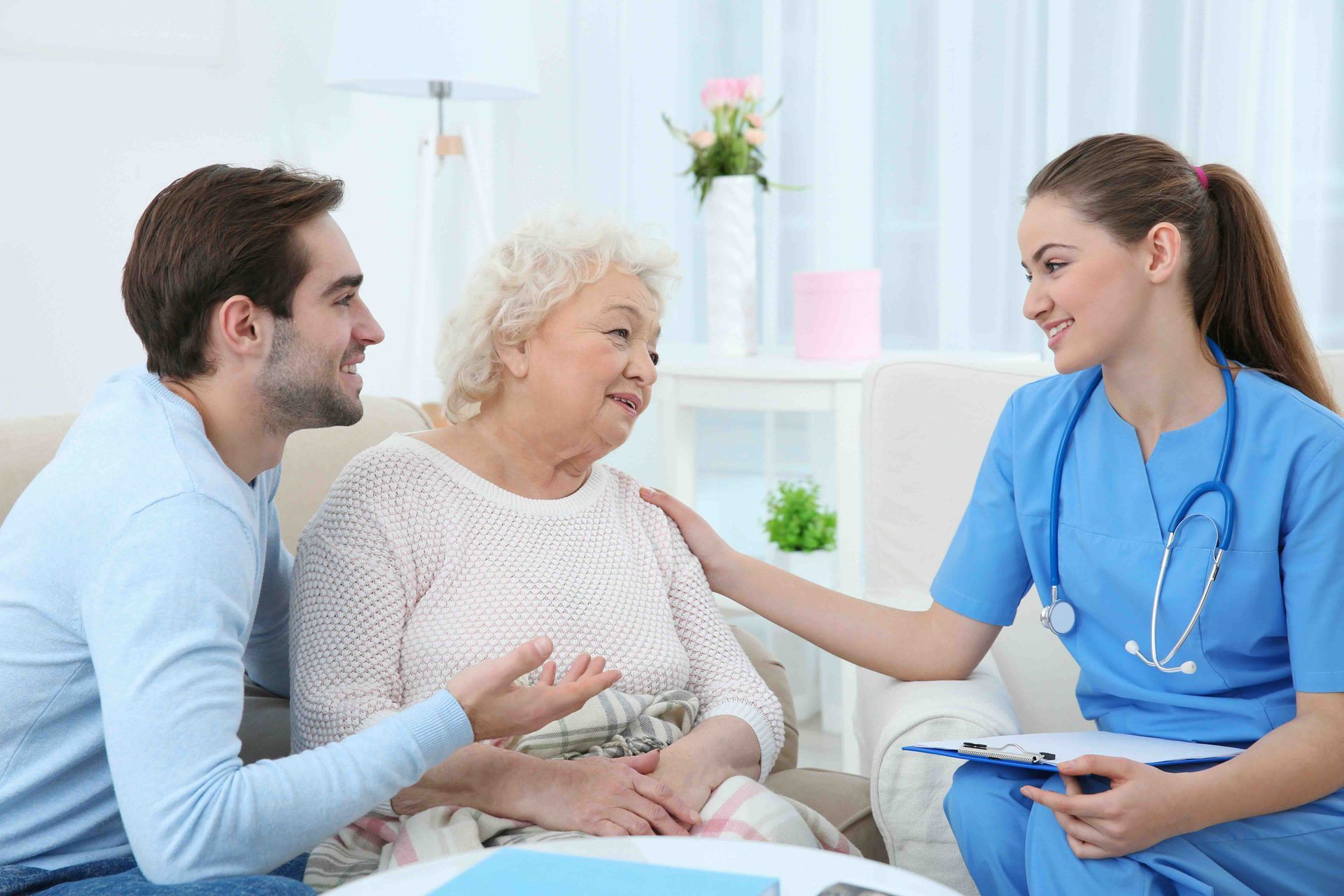 A younger man and an older woman are sitting on a couch talking to a nurse.