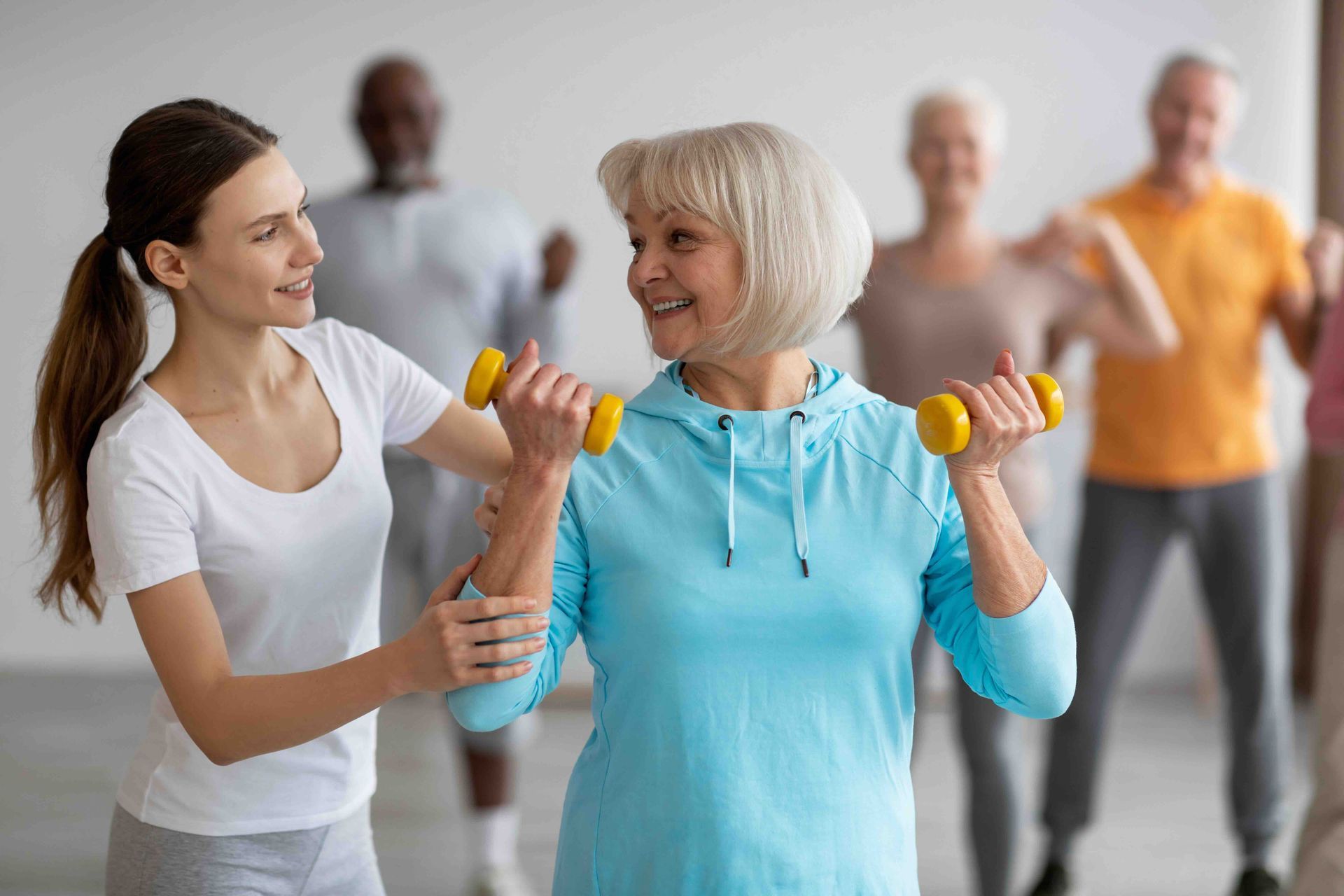 A woman is helping an older woman lift dumbbells in a gym.