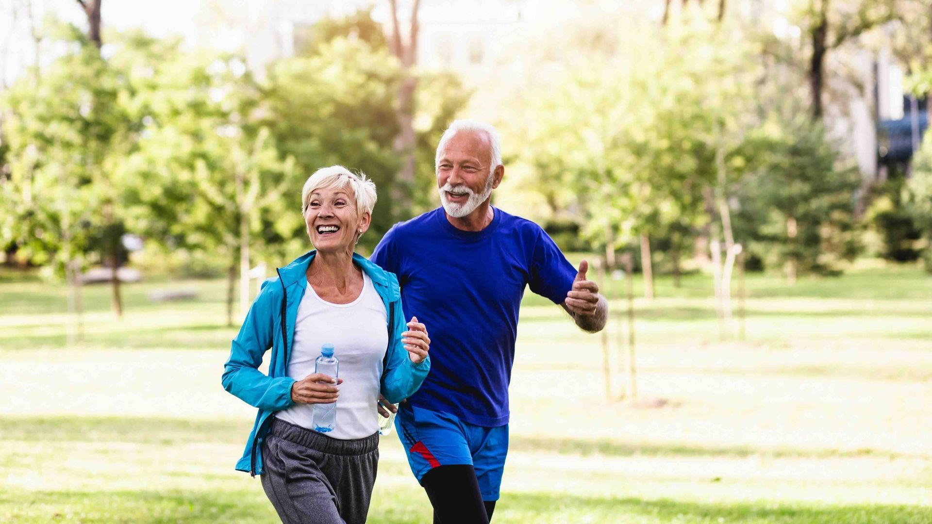 An elderly couple is jogging in a park.