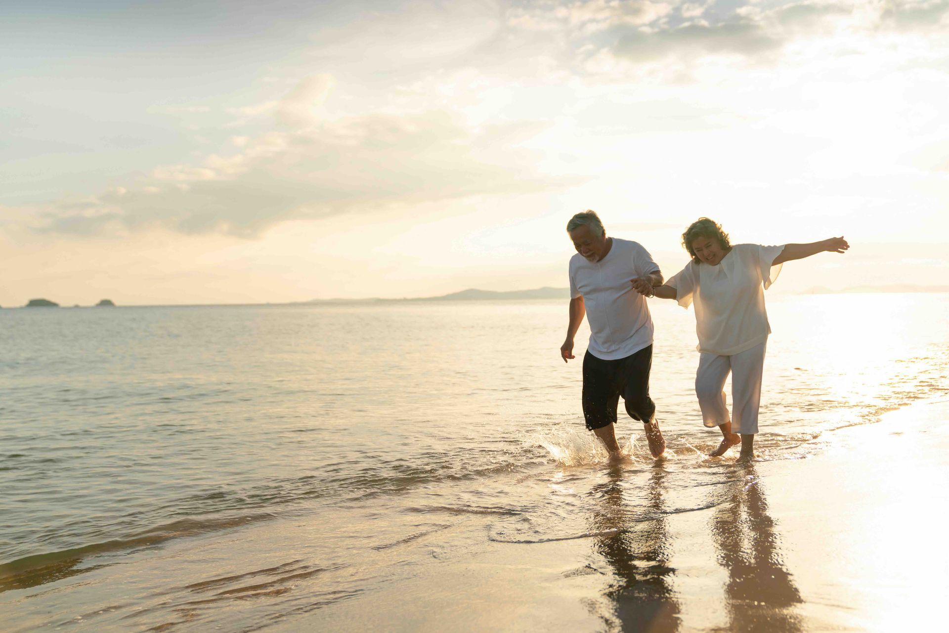 An elderly couple is running on the beach at sunset.