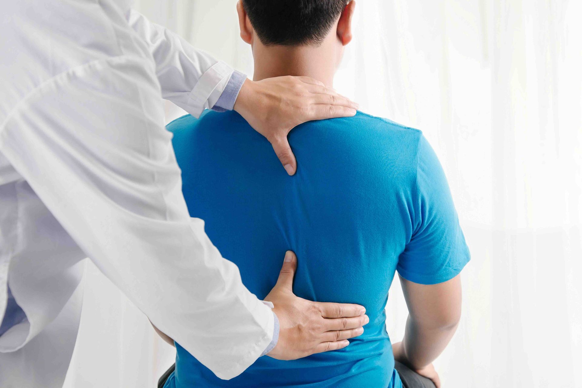 A man in a blue shirt is getting his back checked by a doctor.