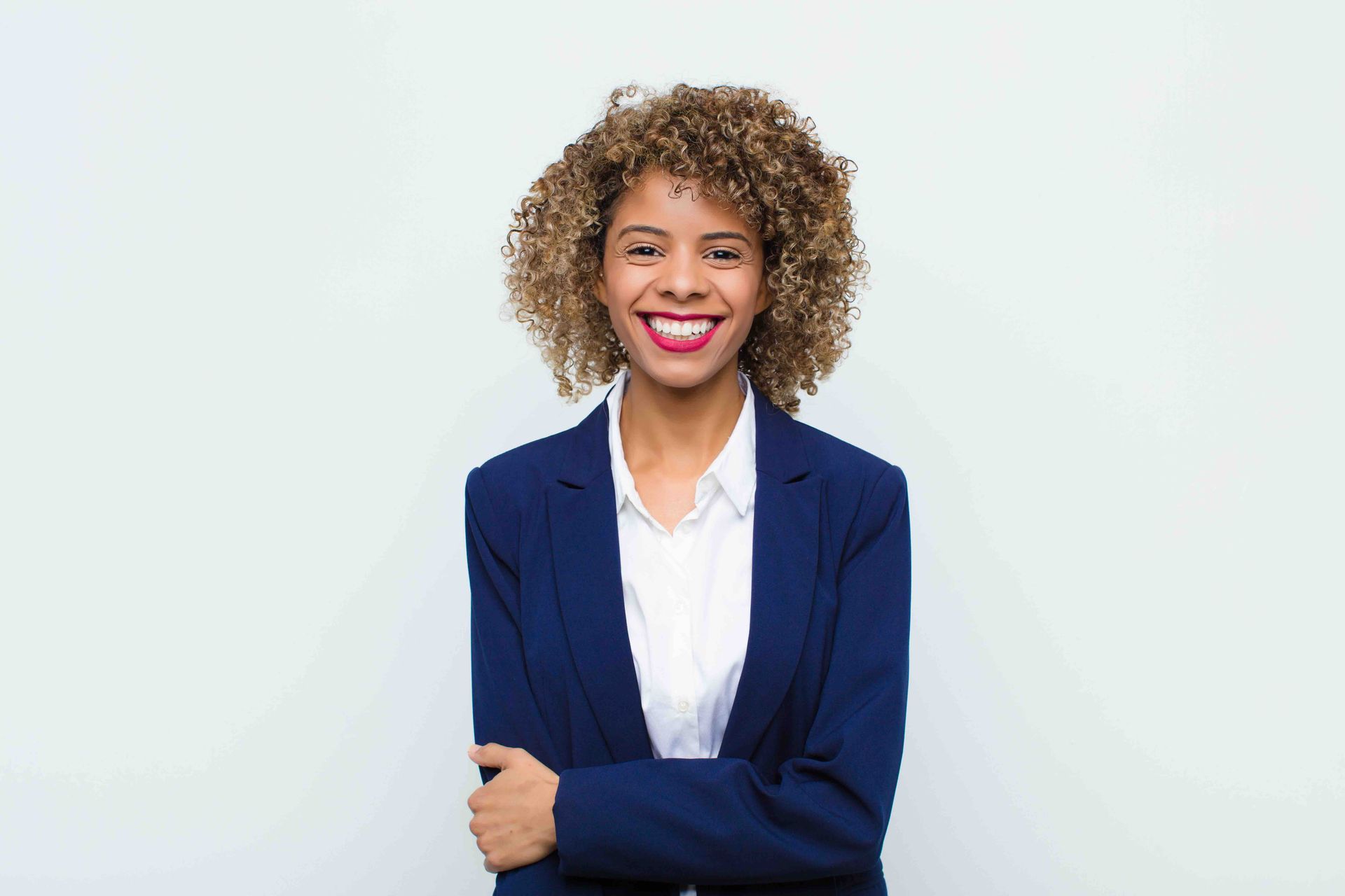 A smiling person with curly hair wearing a navy blue blazer and white collared shirt against a plain white background.