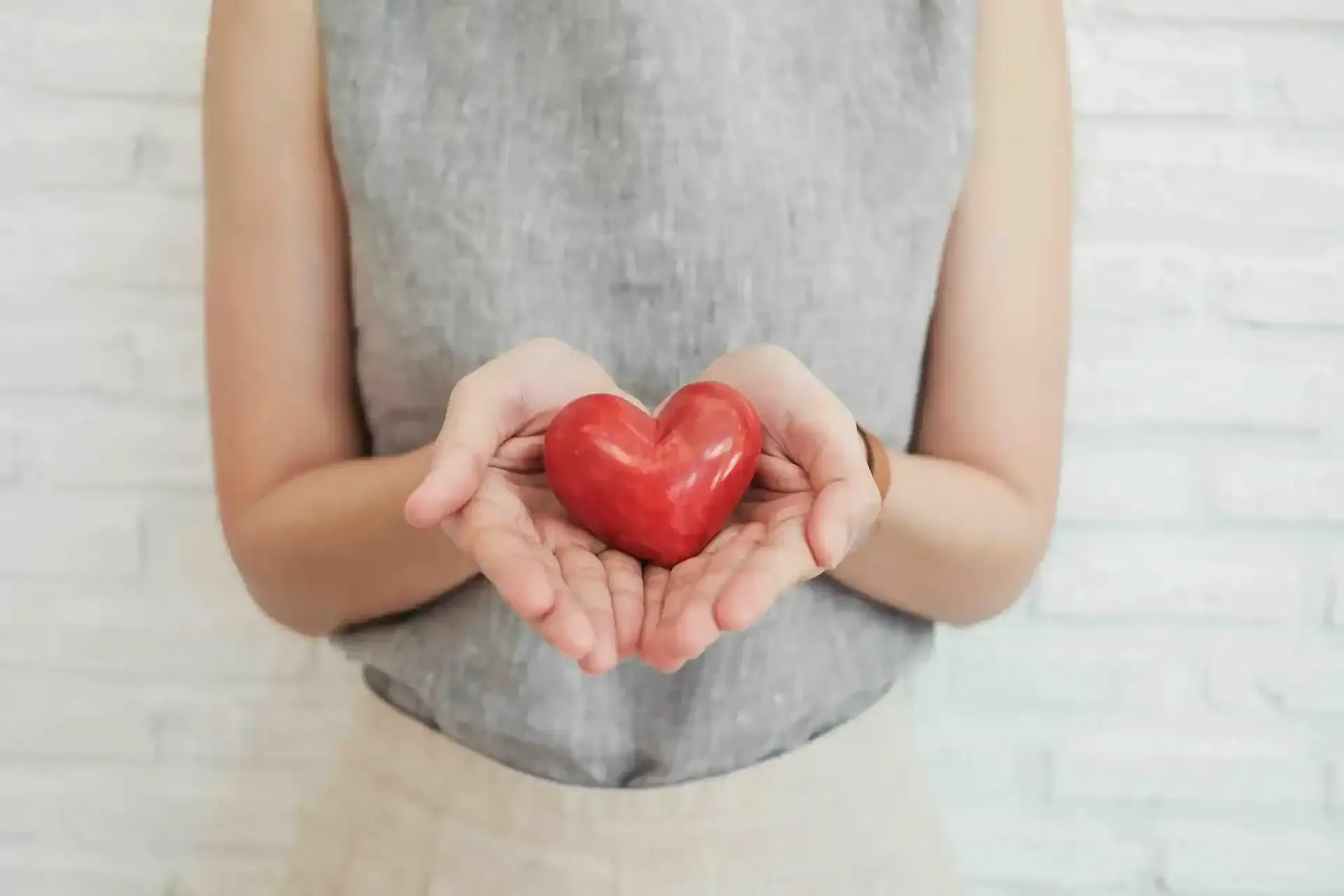 A woman is holding a red heart in her hands.