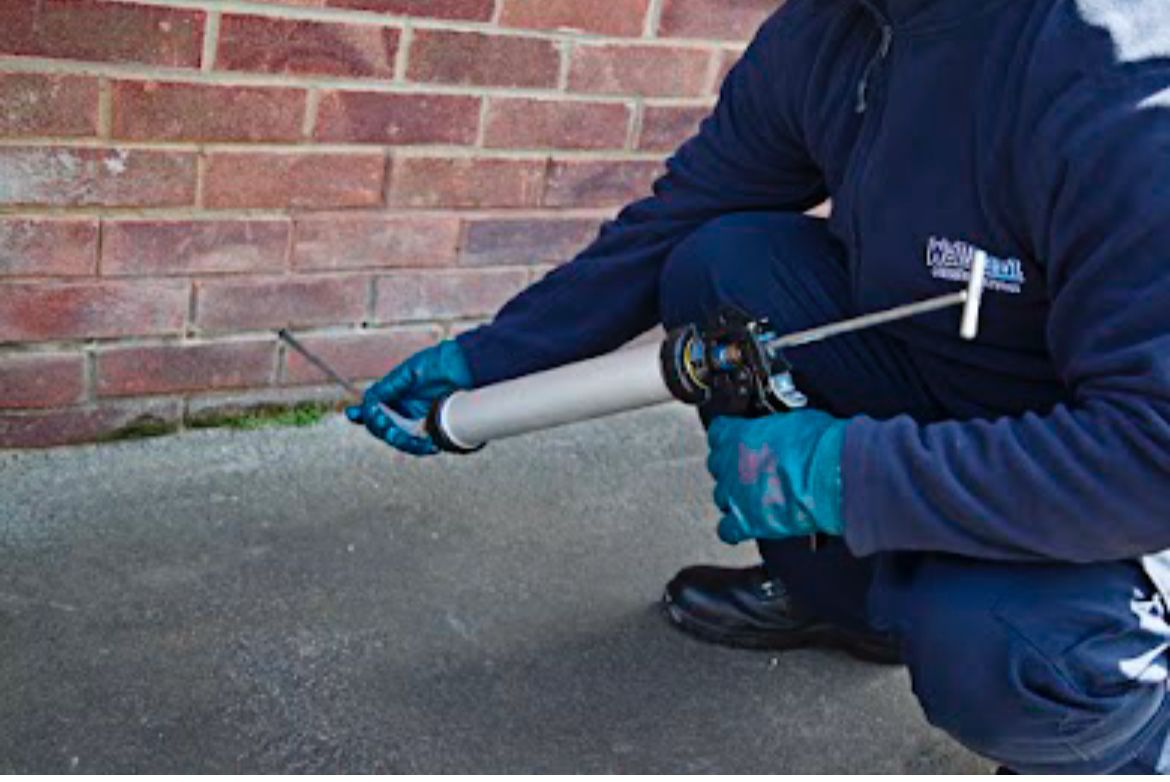 A man in a blue jacket is plastering a wall with a trowel.