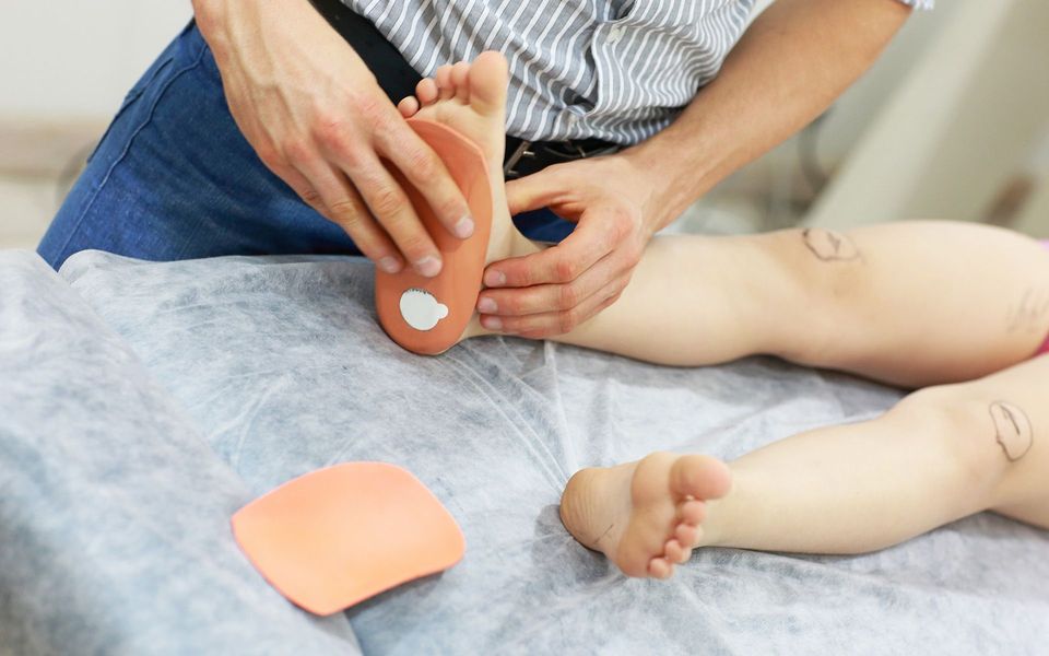 Person fitting a pink orthotic insert into a foot on a table.