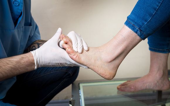 Person's foot being examined by a doctor wearing gloves. Jeans, skin, and examining table.