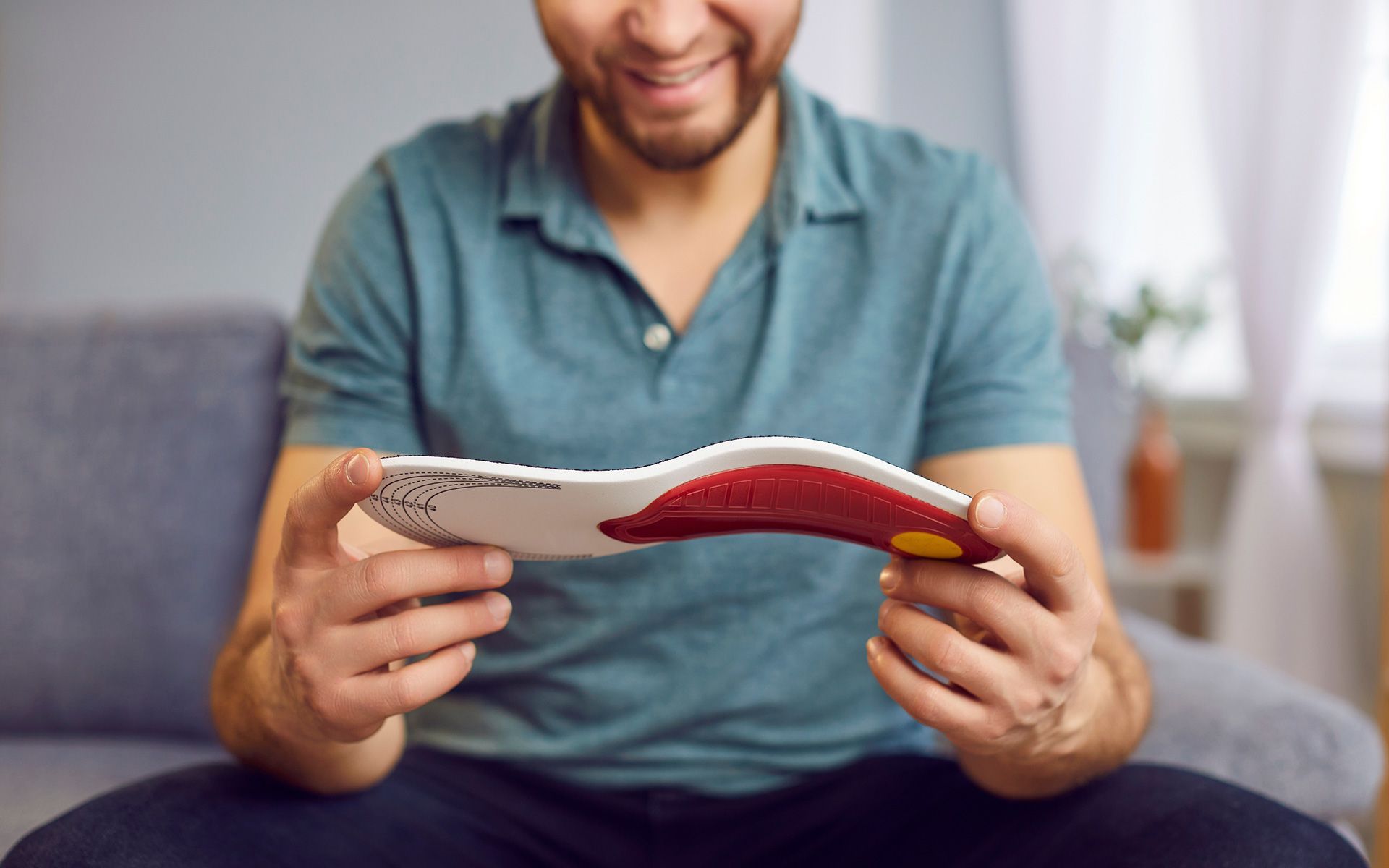 Man seated, smiling, holding an insole with red, white, and yellow sections.