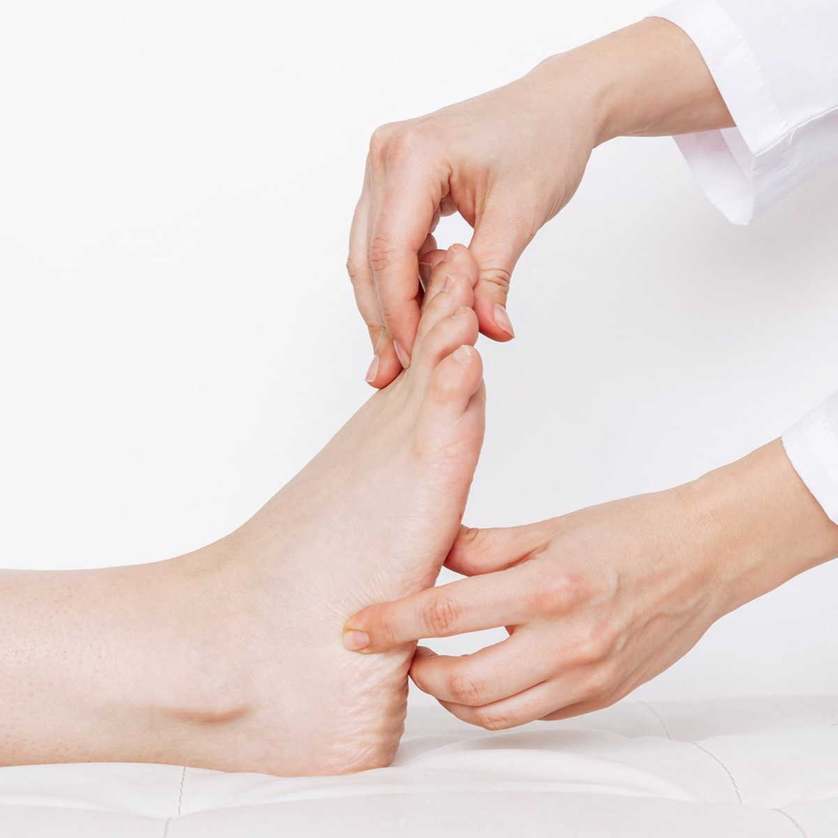 Hands examining a foot on a white surface, possibly for medical assessment.