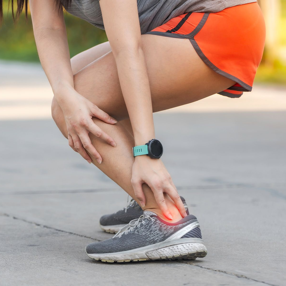 Woman clutching her ankle in pain while wearing running shoes. Red highlight indicates injury.