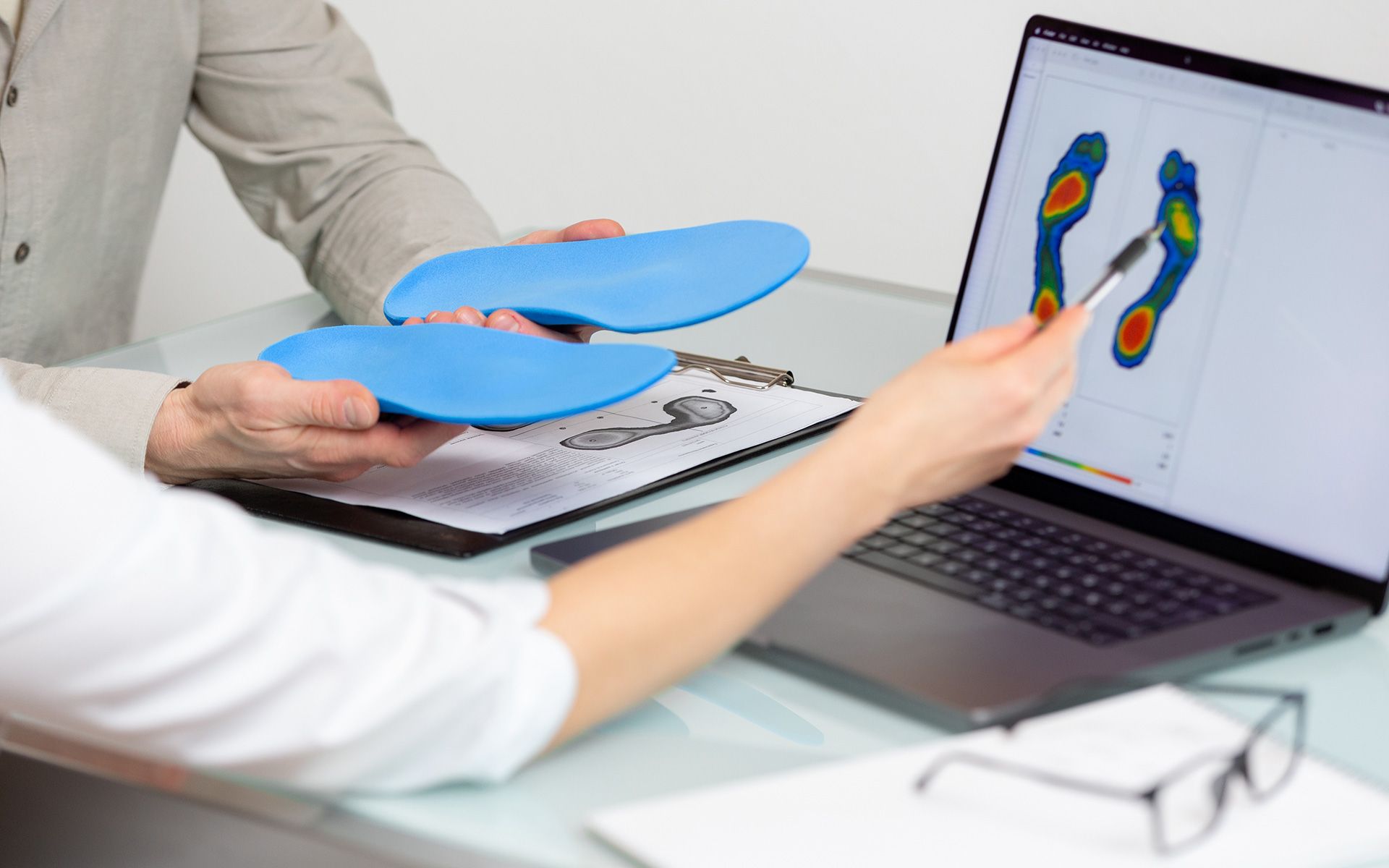 Person pointing at foot pressure scan on laptop, comparing with blue orthotics.