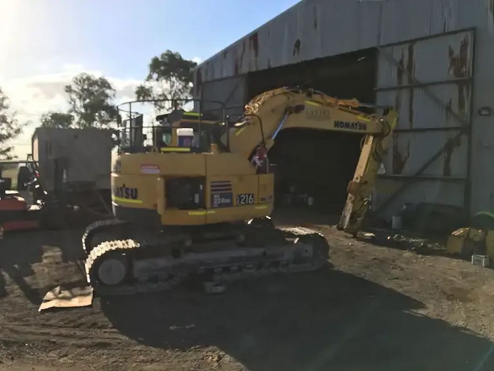 A Yellow Excavator is Parked in Front of a Building — Lantry Earthmoving in Phoenix Park, NSW