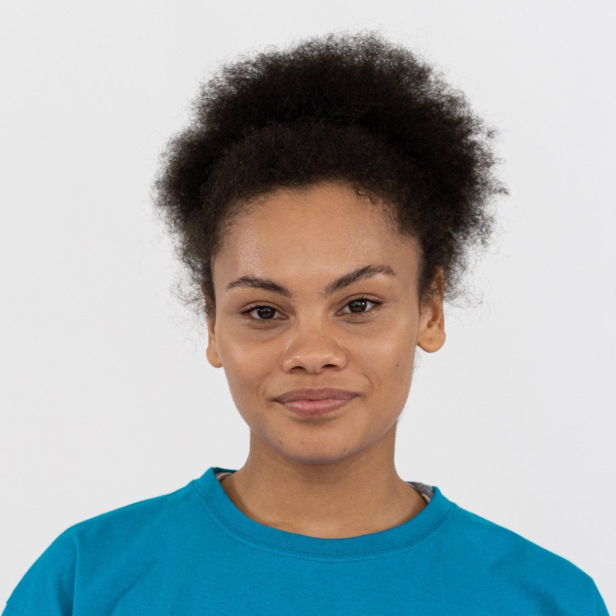 Mulher de cabelos escuros e cacheados, usando um moletom azul, sorri sobre um fundo branco.