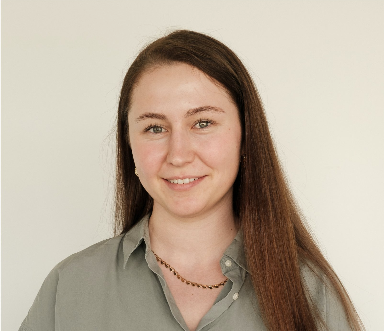 Mulher com longos cabelos castanhos, sorrindo, vestindo uma camisa verde, sobre um fundo branco.