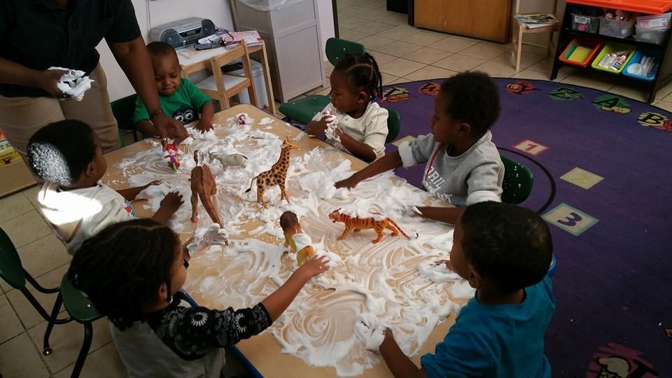 A group of children are playing with shaving cream on a table
