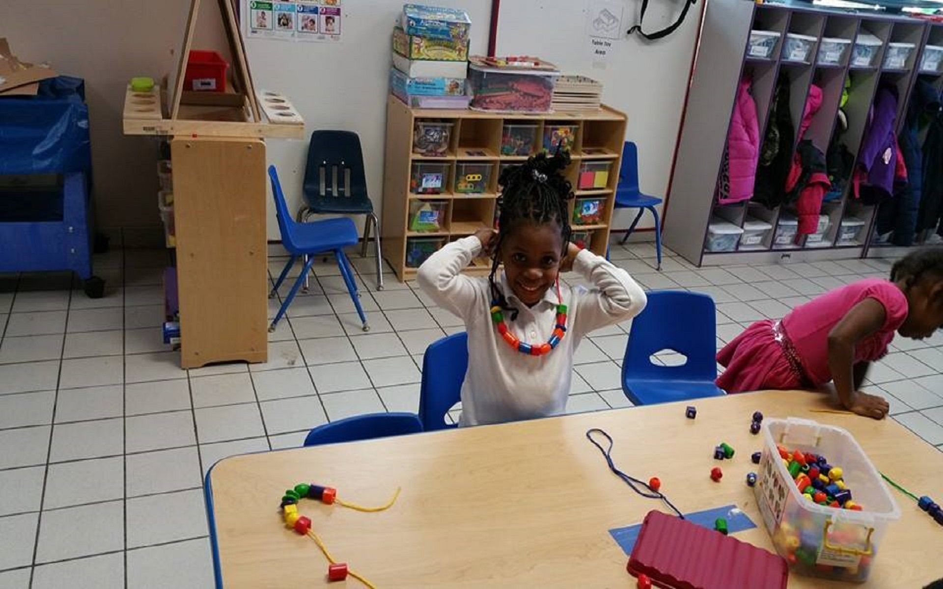A little girl is sitting at a table with beads on it.