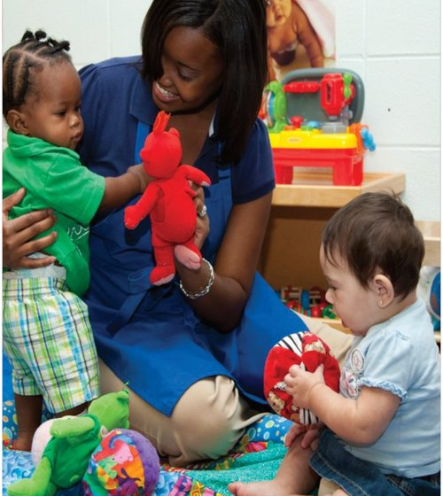 A woman is holding a stuffed animal while two children play with toys