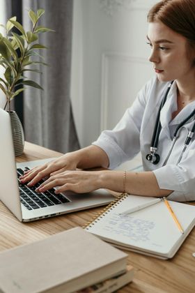 A female doctor is typing on a laptop computer. AI Voice for Health practices.