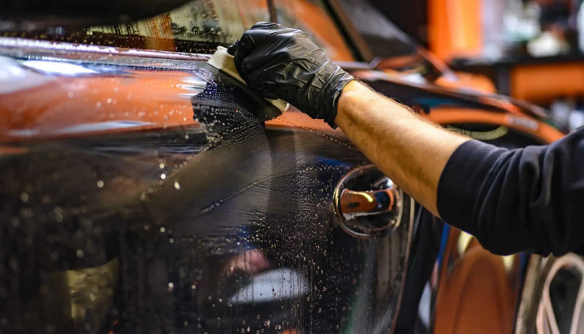 Person washing a black car with a sponge and soapy water.