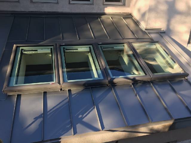 A gray roof with three skylights on it