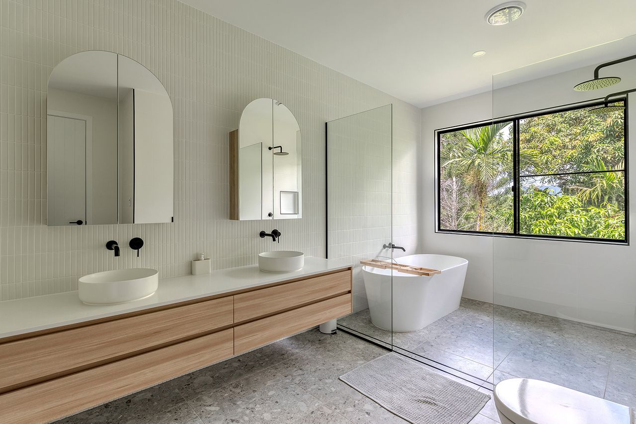 A bathroom with two sinks , a tub and a window.