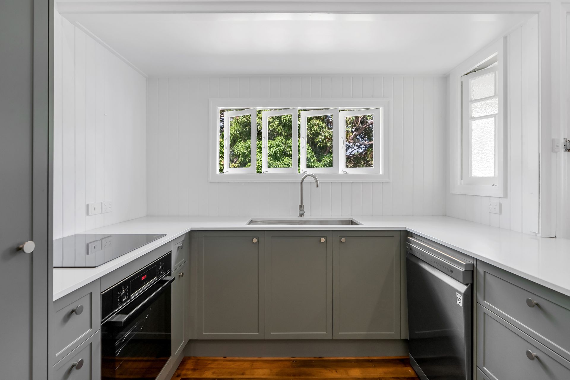 A kitchen with gray cabinets , a stove , a sink , and a window.