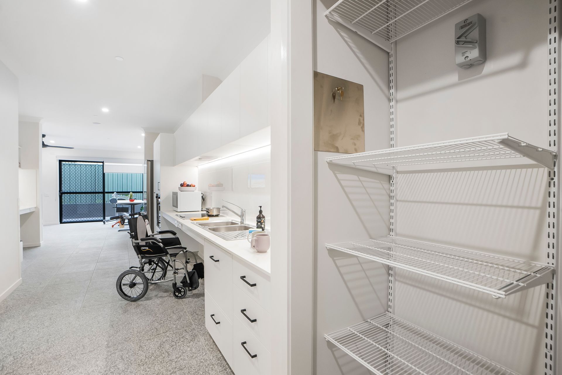 A wheelchair is parked in a kitchen next to a shelf.
