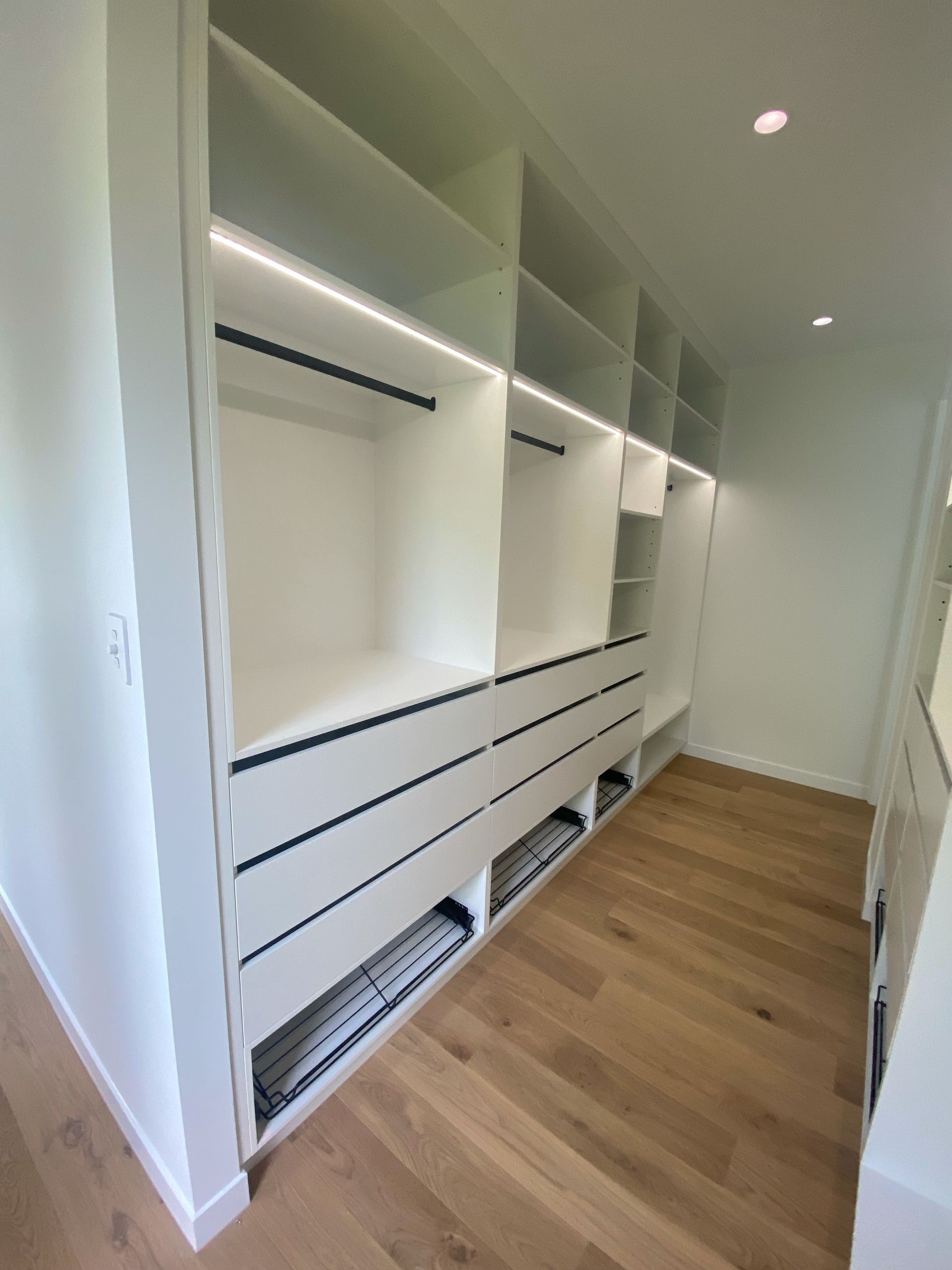 A walk in closet with wooden floors and white shelves.