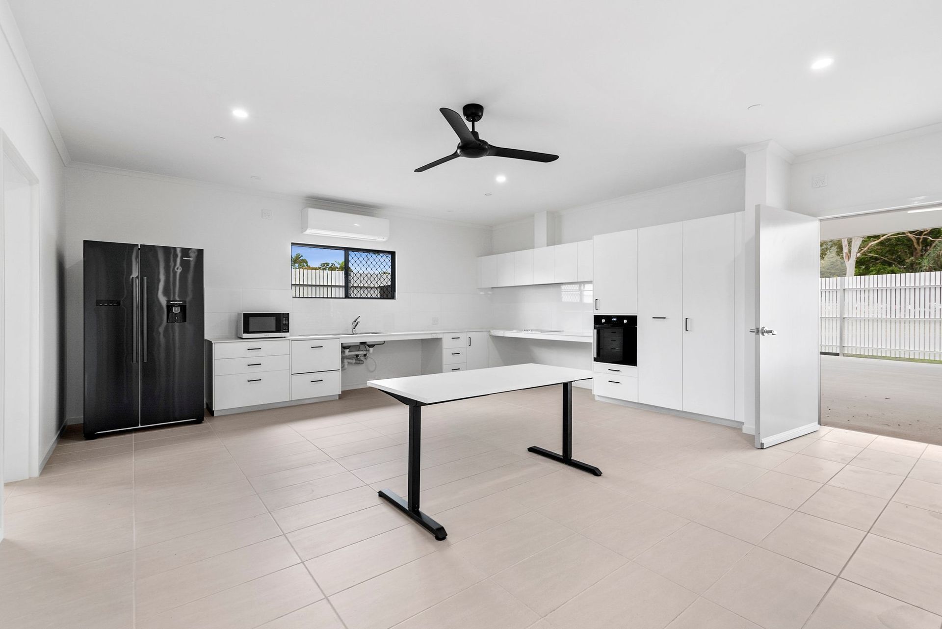 A kitchen with white cabinets , a black refrigerator , a table and a ceiling fan.