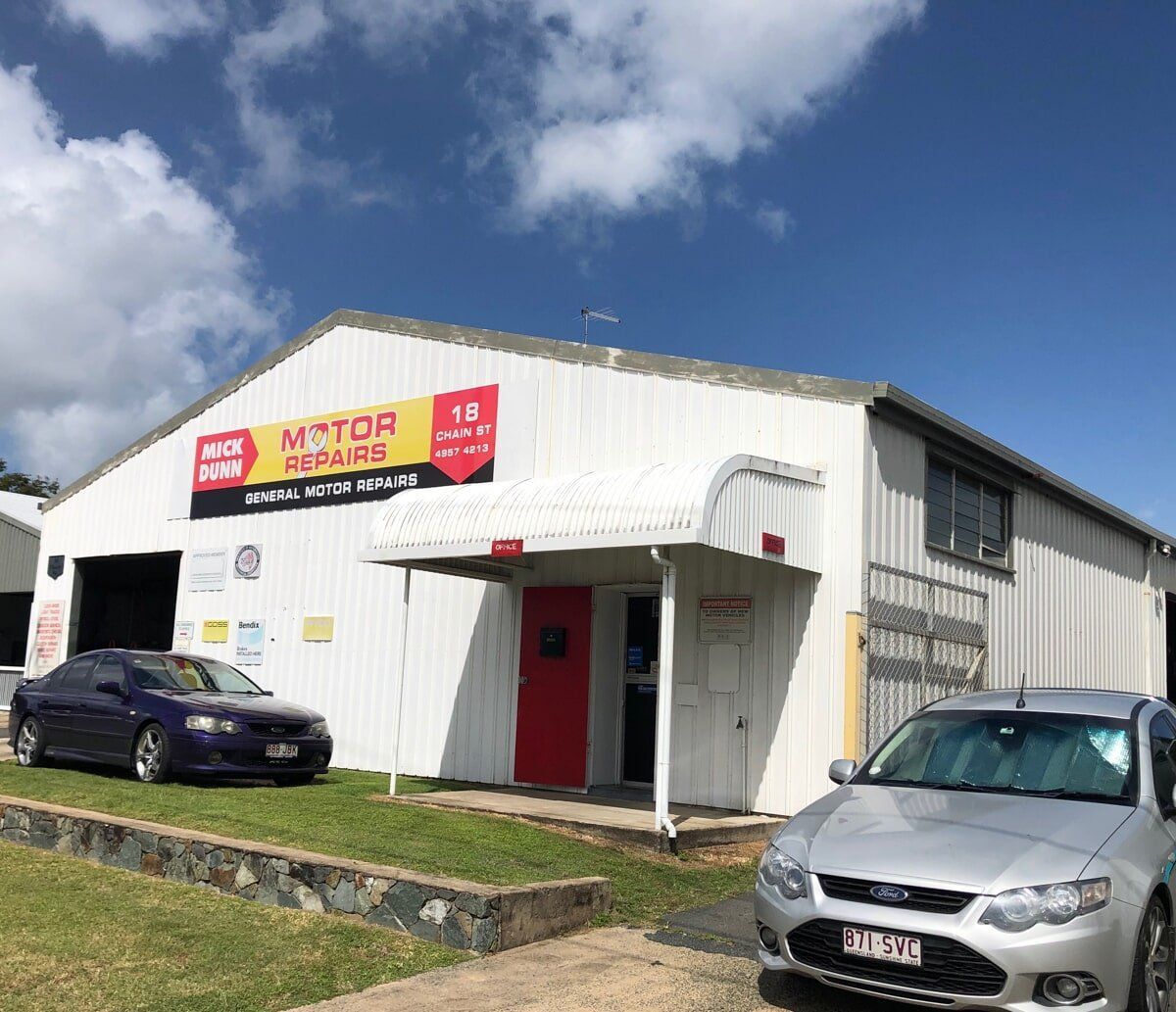 Two Cars Are Parked in Front of a White Building — Mick Dunn Motor Repairs in Mackay, QLD
