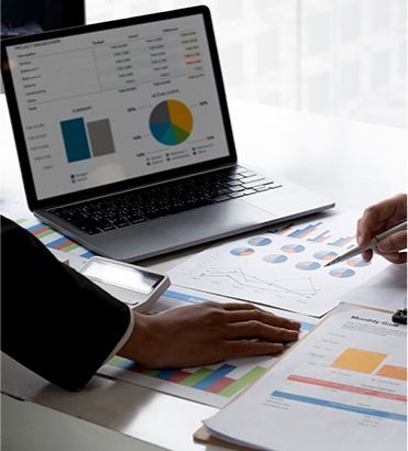 Two people reviewing financial data on a laptop and printed charts.