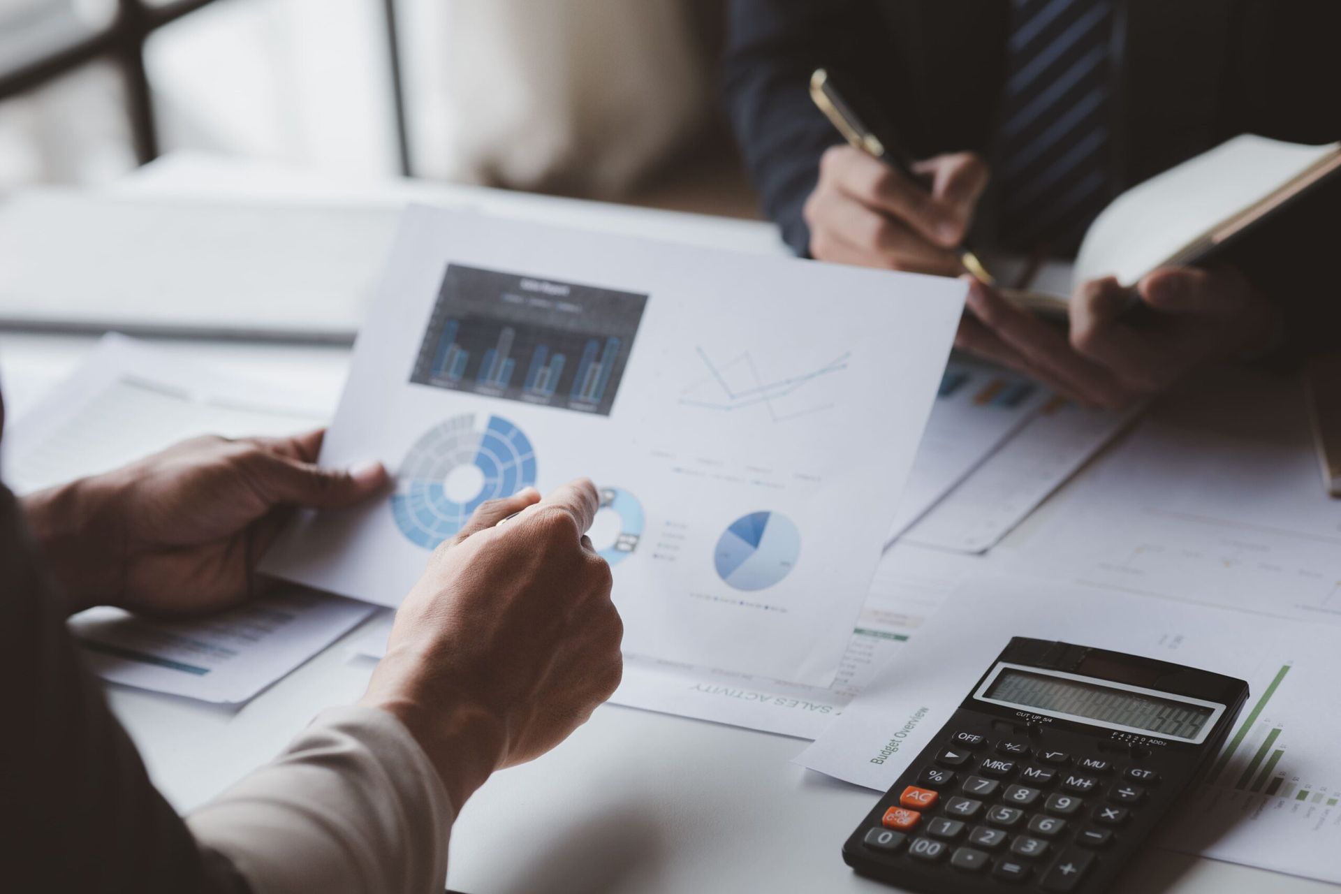 Two people reviewing financial charts and data, using a calculator.