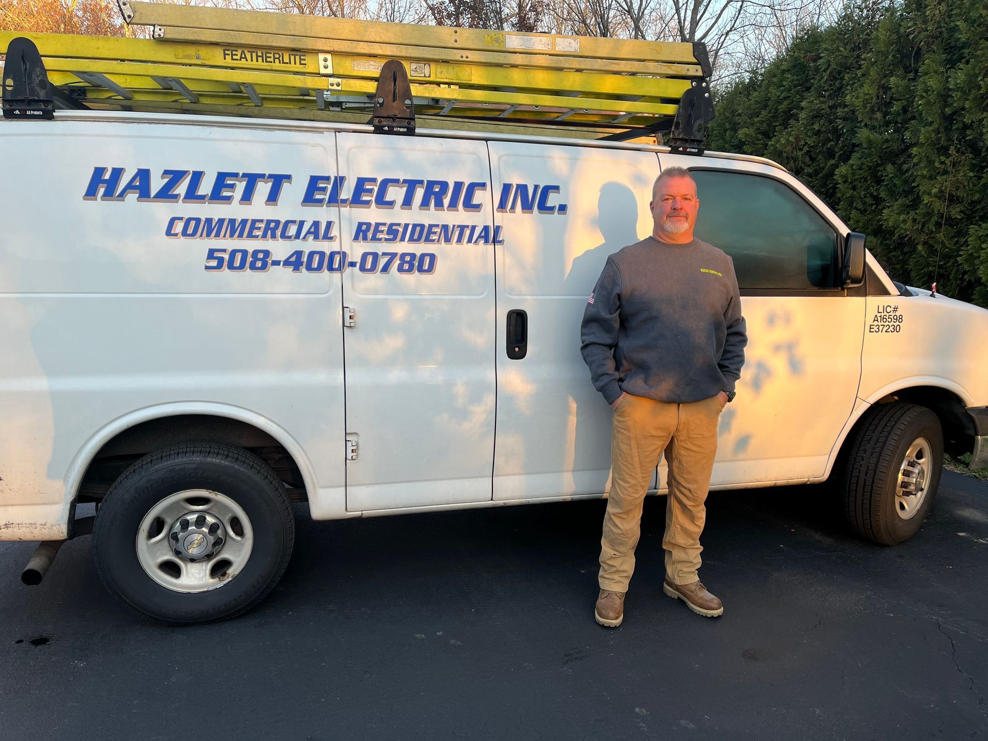 A man is standing in front of a hazlett electric inc. van.
