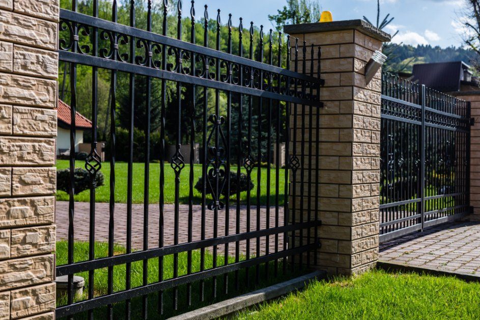 A Black Wrought Iron Fence Surrounds a Brick Wall and A Driveway — Glass Pool Fencing Australia in Smiths Lake, NSW