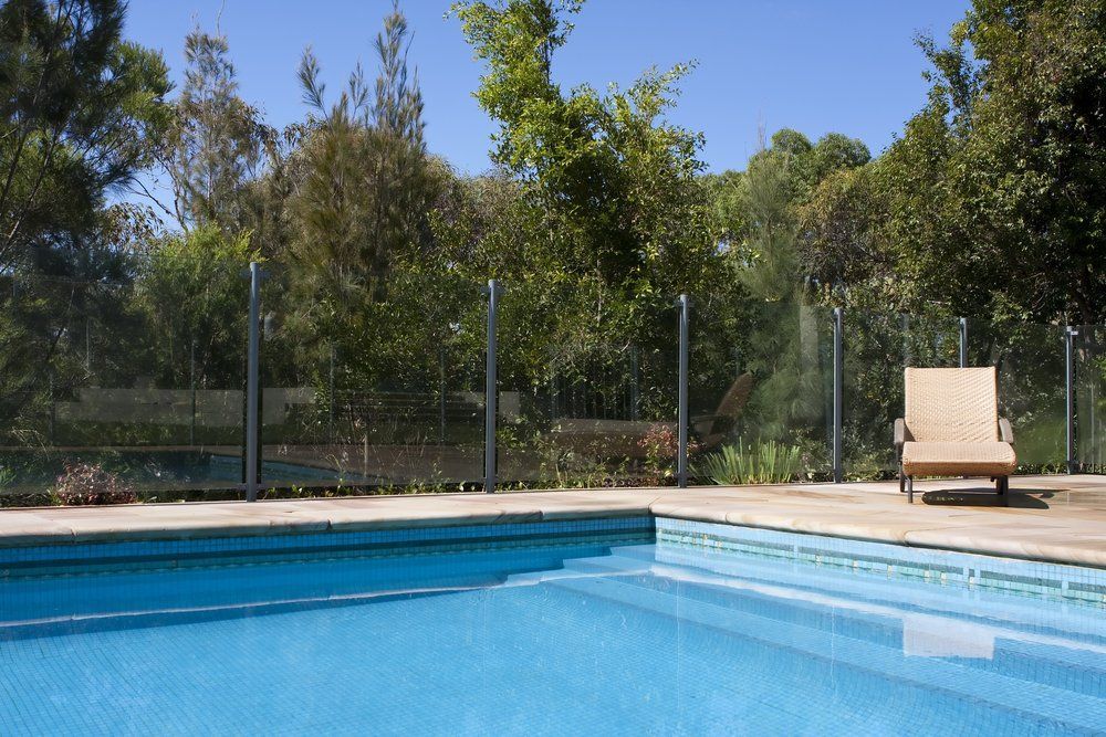 A Swimming Pool with A Chair and Trees in The Background — Glass Pool Fencing Australia in Wingham, NSW