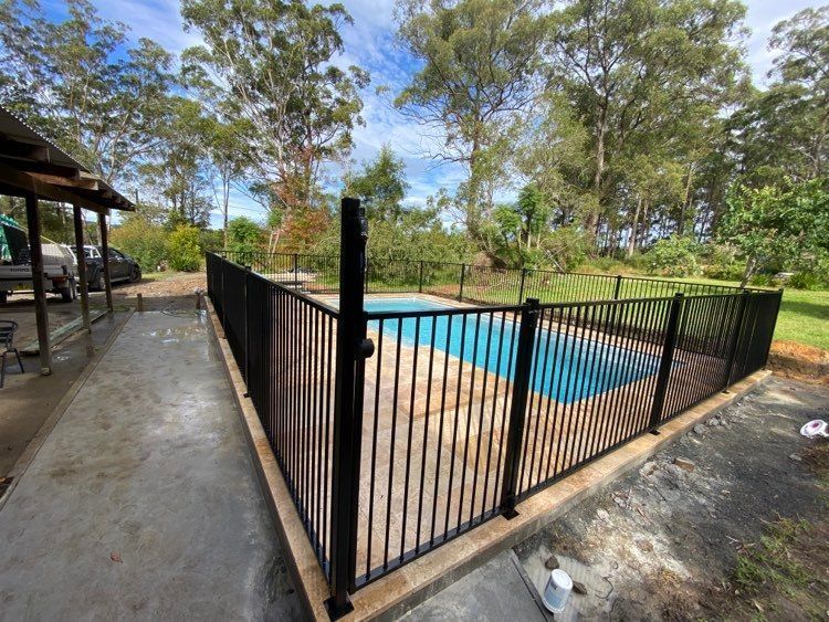 A Large Swimming Pool Surrounded by Chairs and A Fence — Glass Pool Fencing Australia in Laurieton, NSW