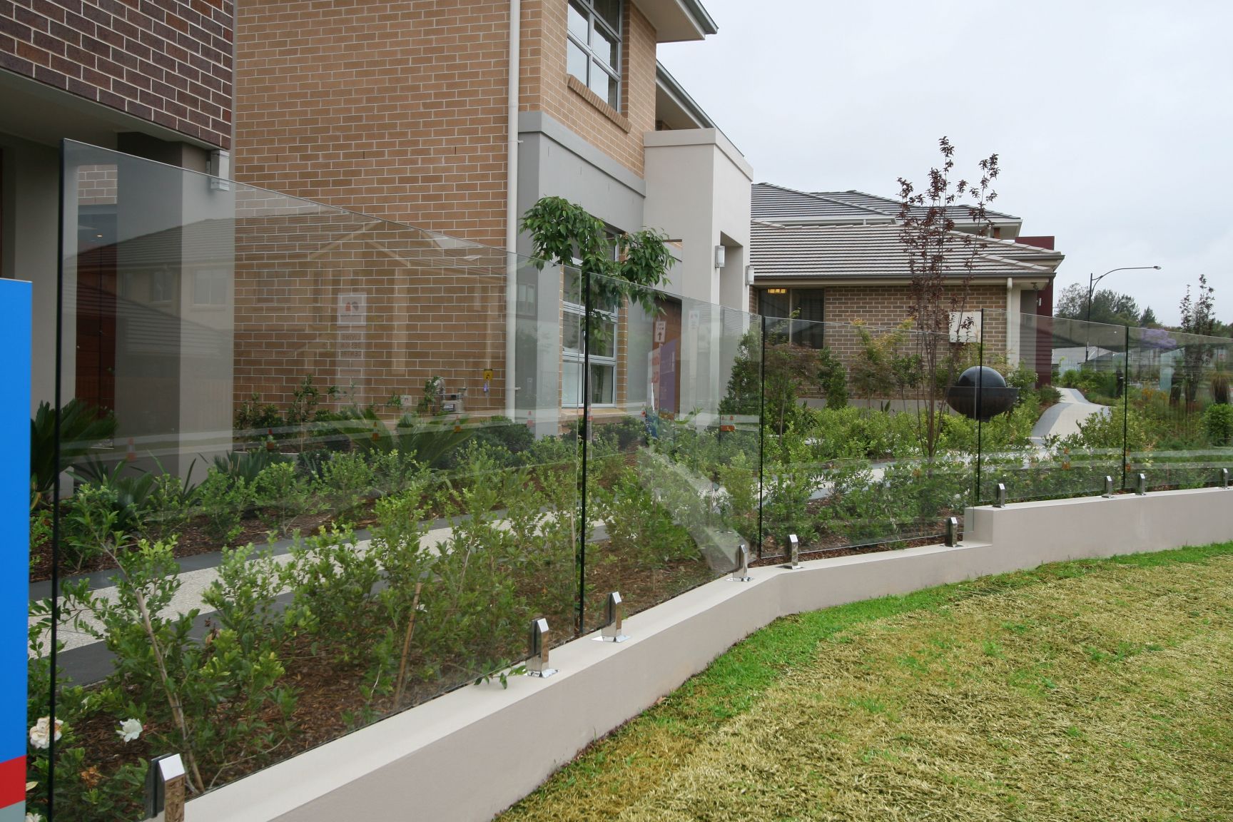 A Glass Fence Sits Atop a Curved Light-Colored Retaining Wall — Coastline Glass Pool Fencing in Old Bar, NSW