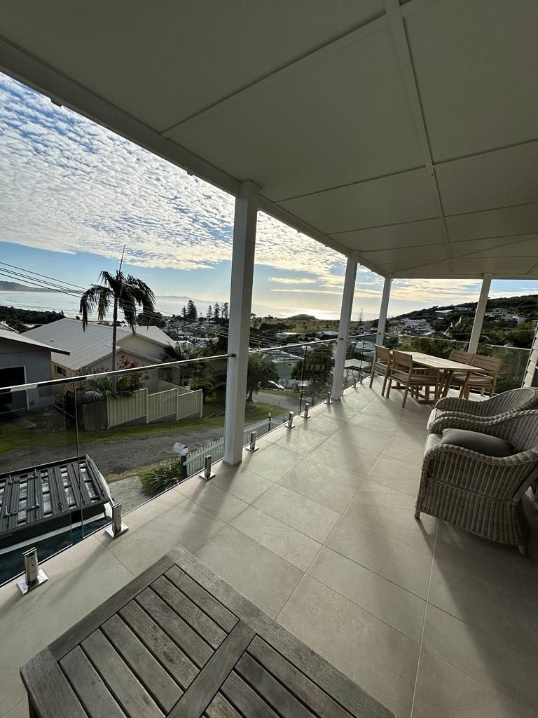 A balcony with a table and chairs and a view of a city.— Glass Pool Fencing Australia in Old Bar, NSW