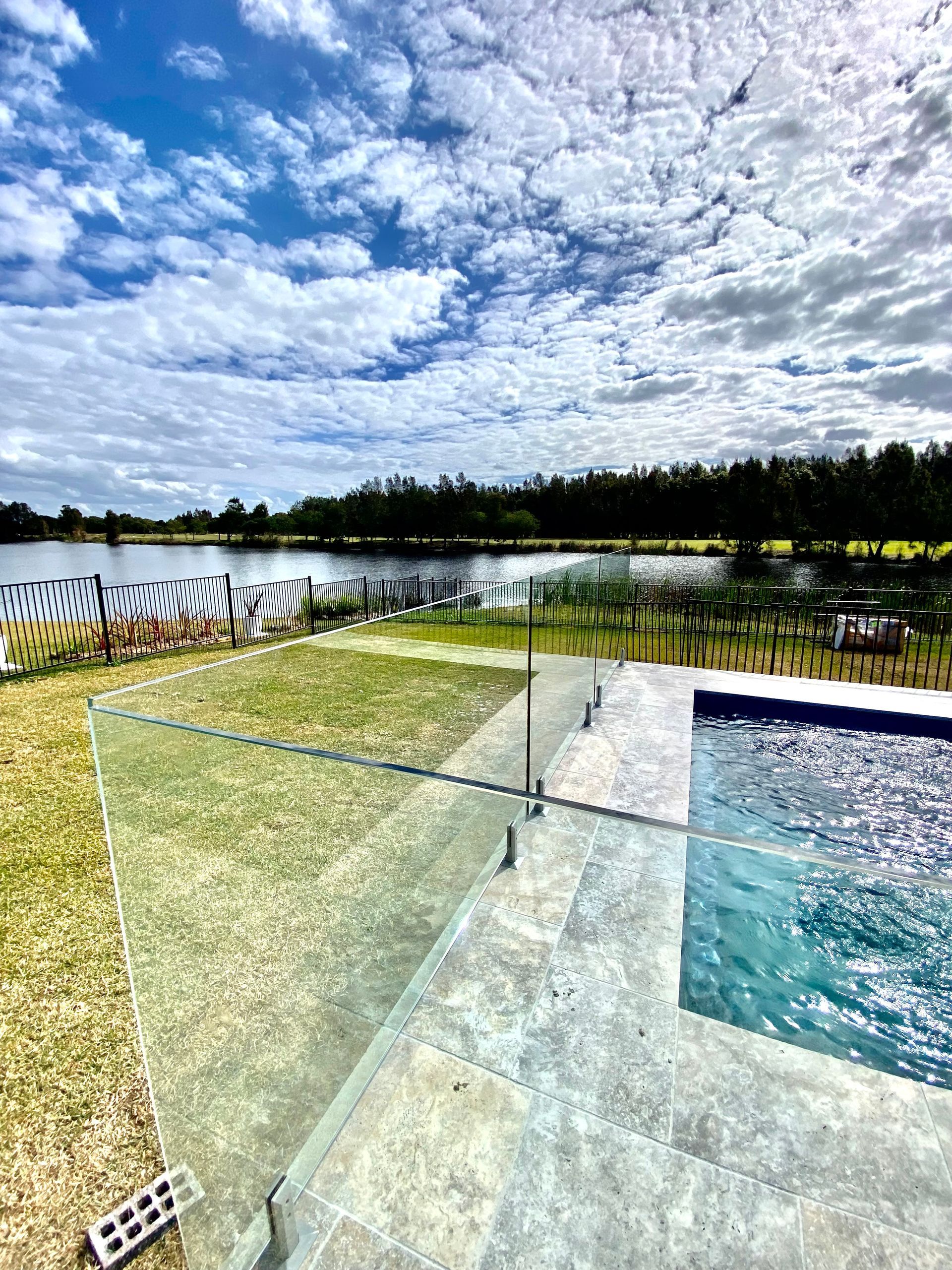 A swimming pool with a glass railing and a view of a lake. — Glass Pool Fencing Australia in Old Bar, NSW